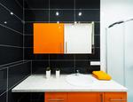 Pomarańczowe meble łazienkowe i czarne płytki ceramiczne – projekt nowoczesnej łazienki